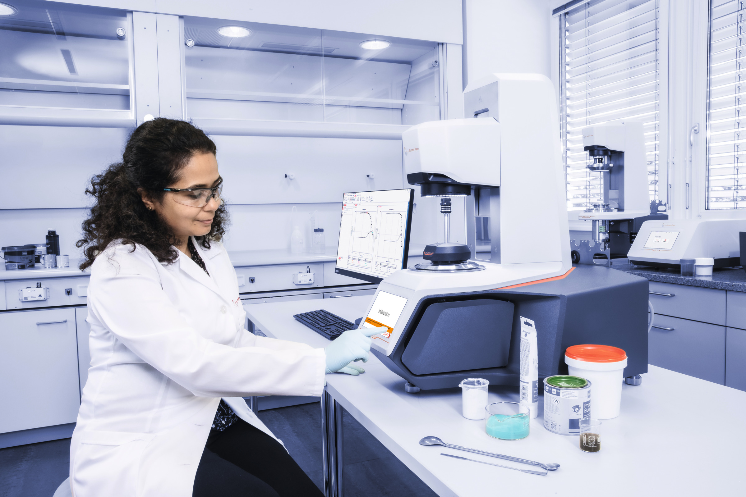 Lab technician uses the touchscreen of an Anton Paar MCR rheometer next to paint samples in a laboratory