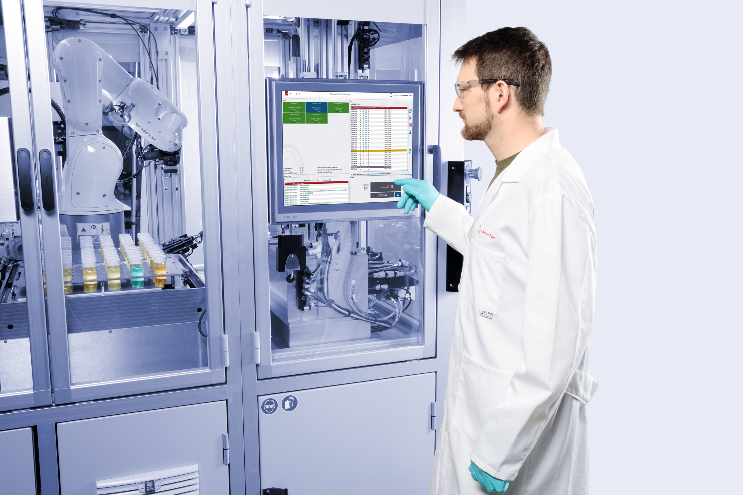 Laboratory technician operating Anton Paar HTR 7000 automated laboratory system with robotic arm and sample bottles in enclosed workspace