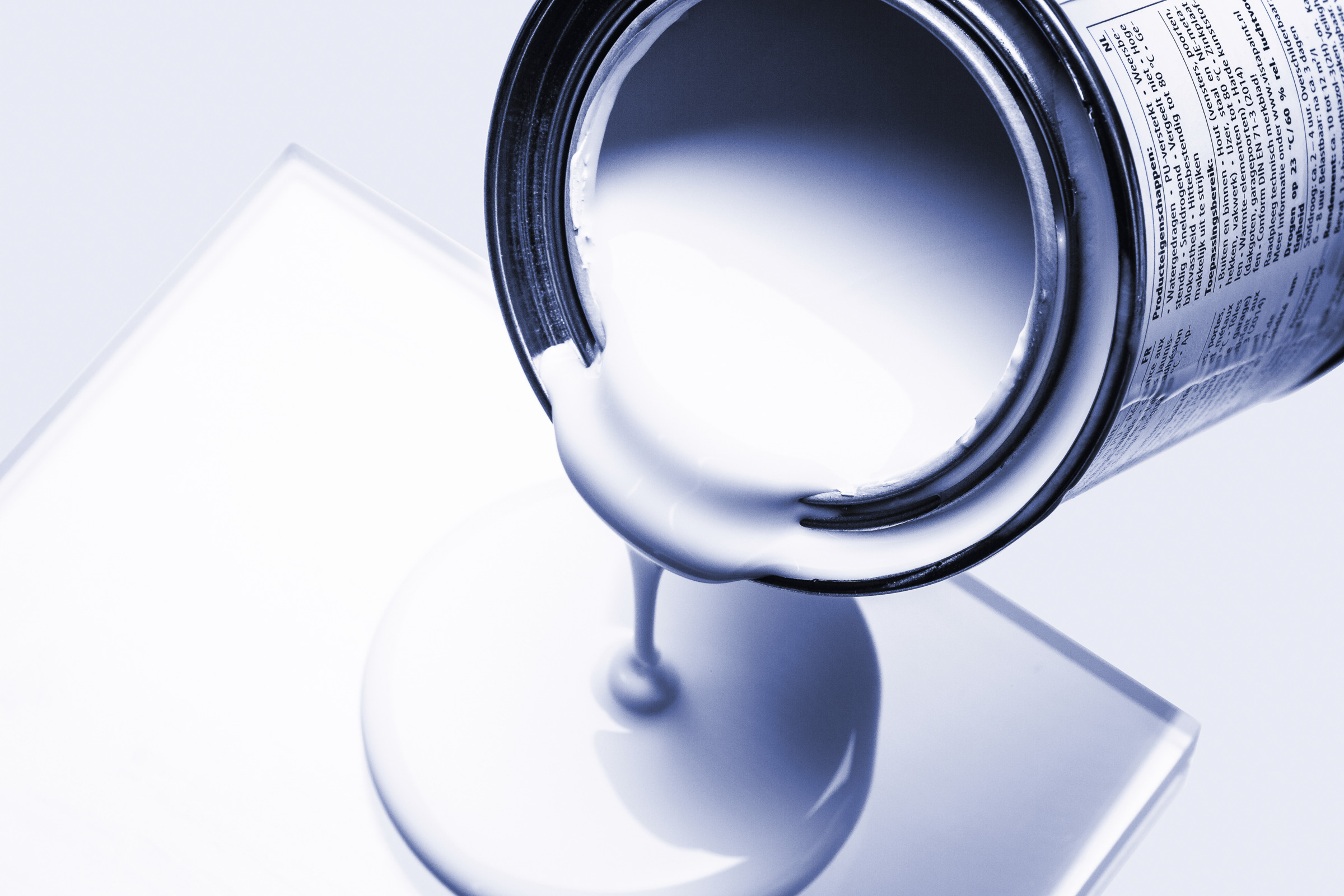 Close-up of white coating material pouring from an open container onto a flat surface during viscosity or formulation testing