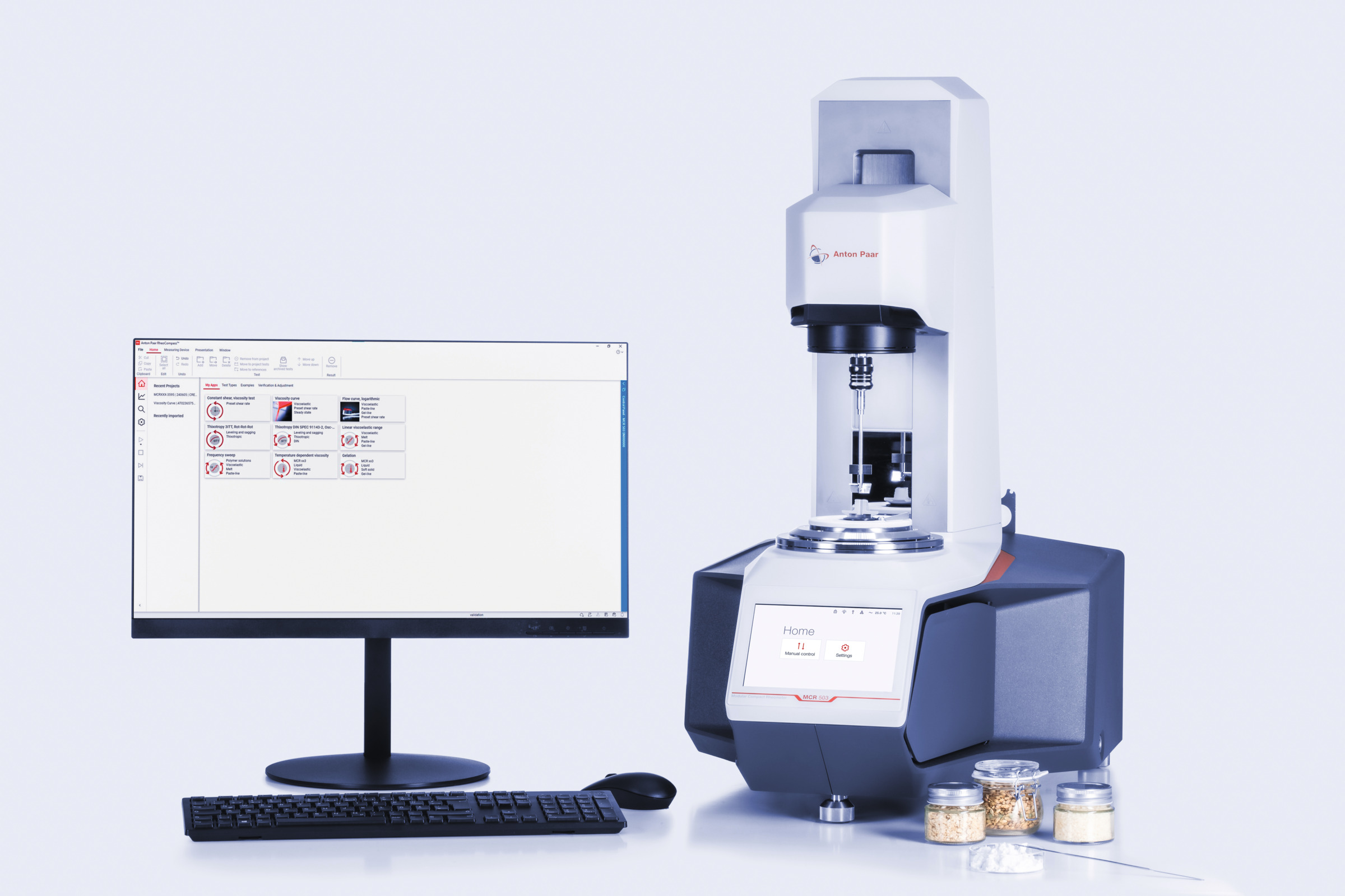 Anton Paar MCR 503 rheometer beside a monitor with RheoCompass software and sample jars on a white surface.