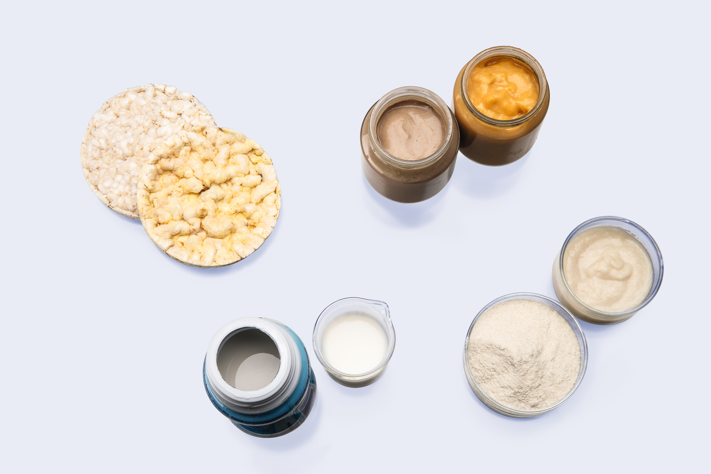 Top view of puffed rice cakes, jars with pastes, a powder sample, and liquid samples on a white surface
