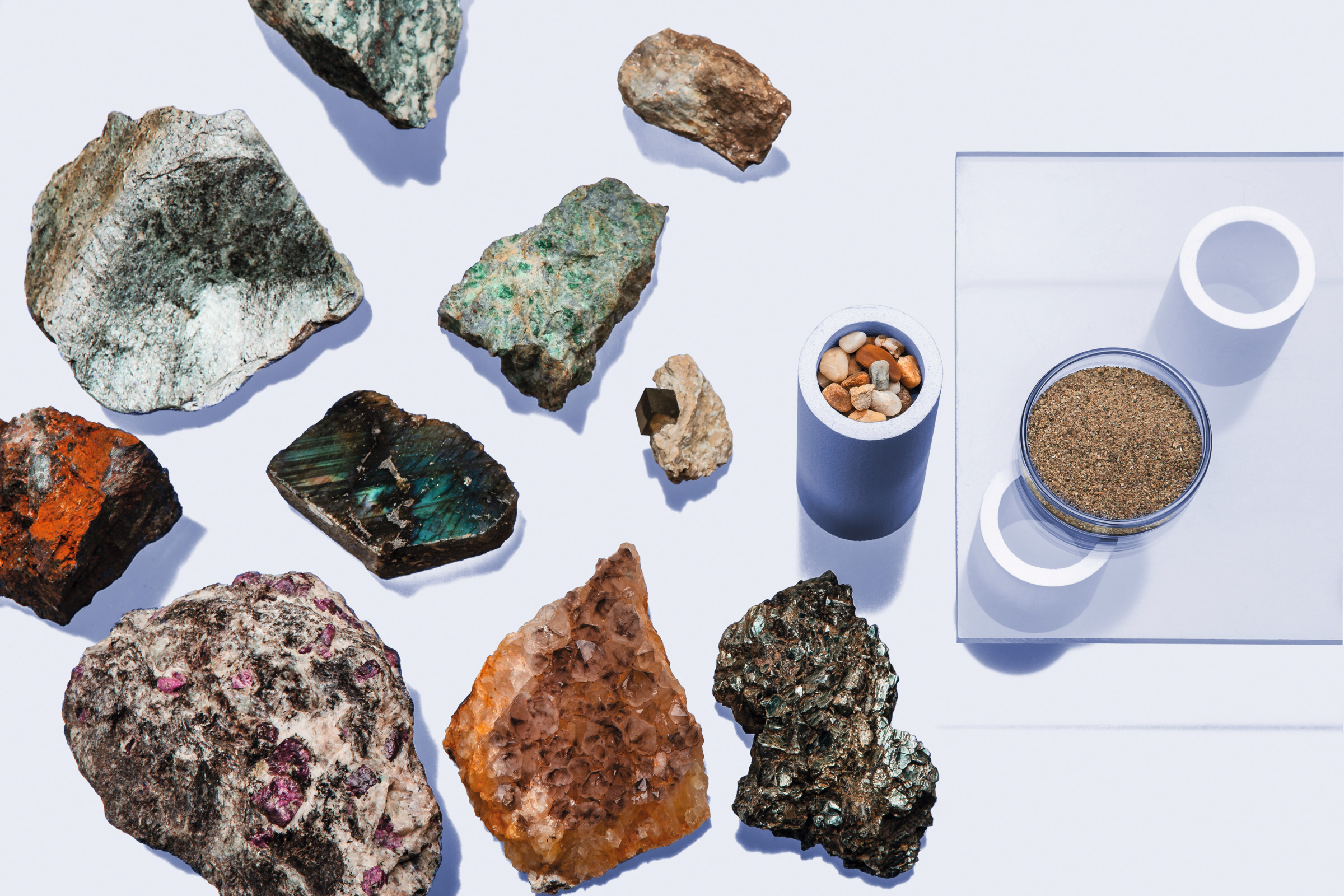 Rock and mineral samples arranged beside dishes of pebbles and sand on a clear acrylic plate