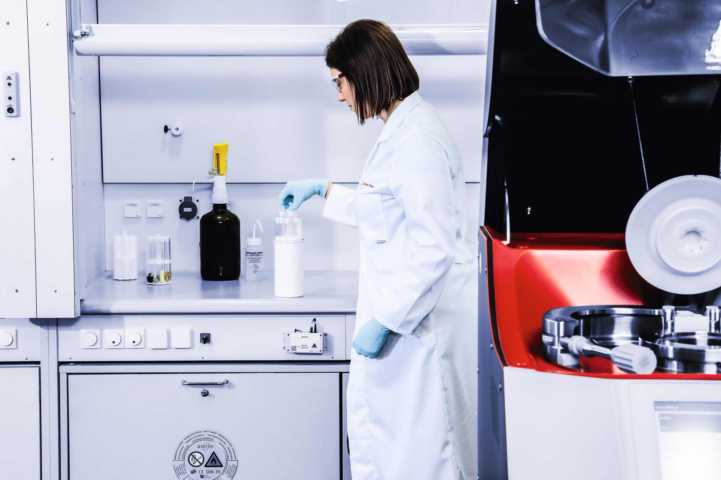 Technician prepares sample vials under a fume hood beside a partially visible Anton Paar Multiwave 7301 microwave digestion system