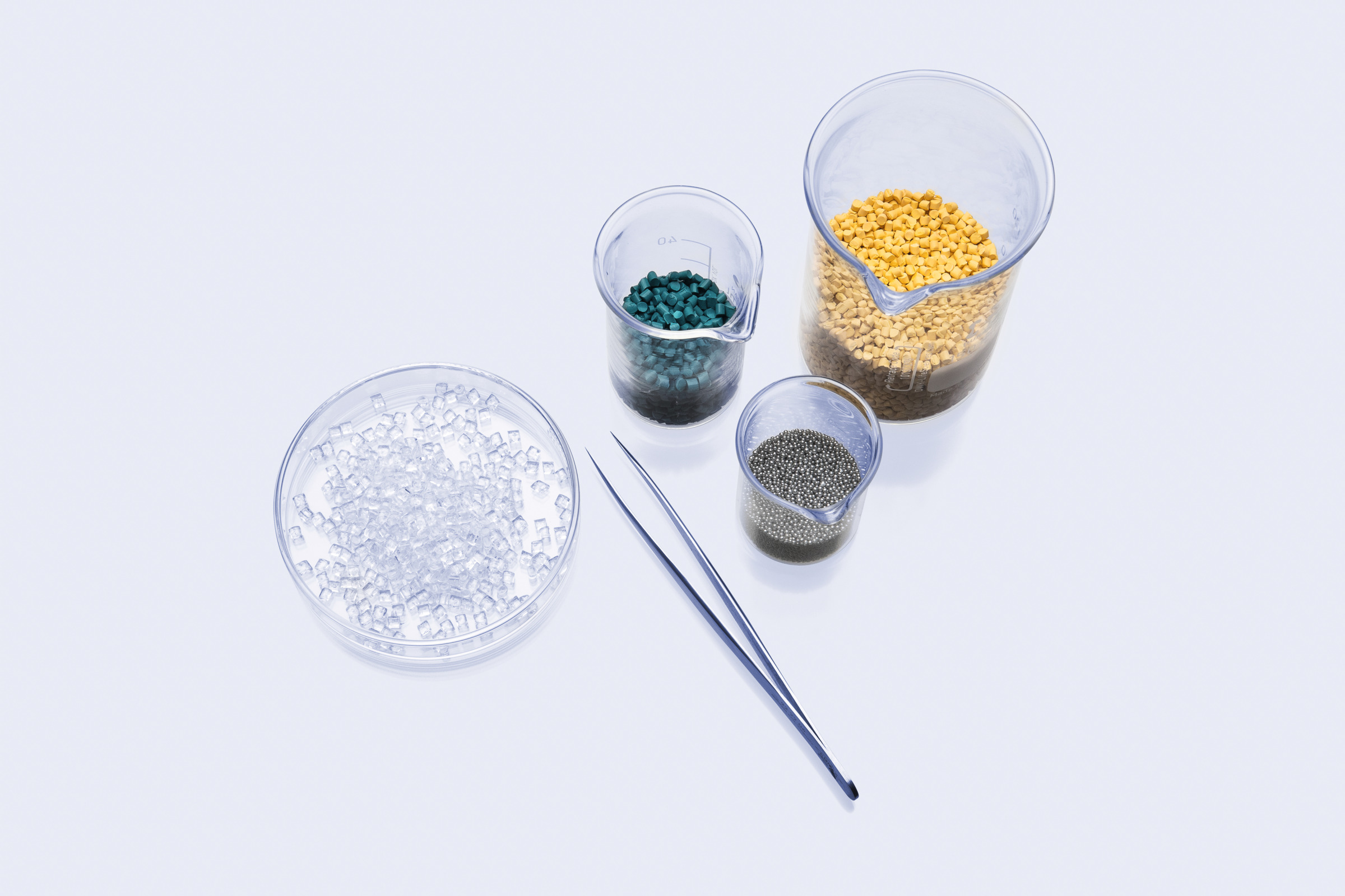 Clear dish, beakers with colored plastic pellets and metal beads, and tweezers on a light background