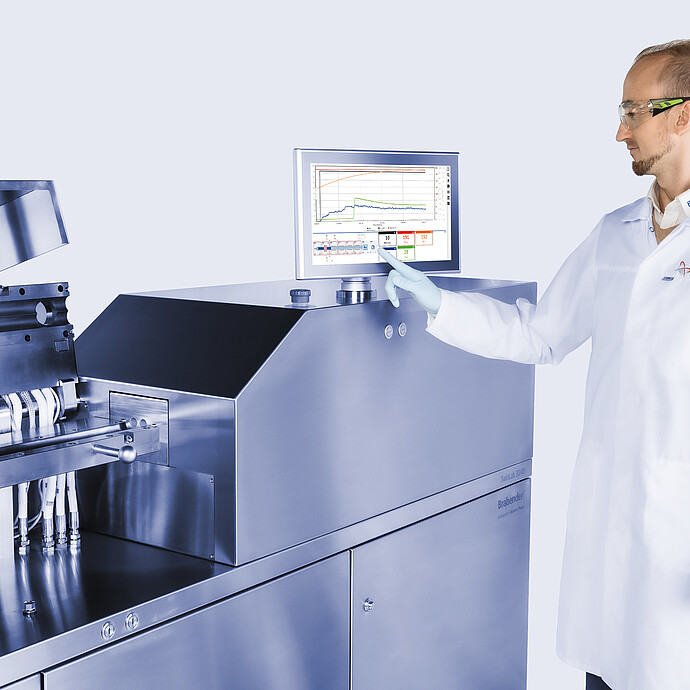 Technician operating Brabender TwinLab B-TSE-S-30-40 twin-screw extruder, adjusting touchscreen while process section with piping is open