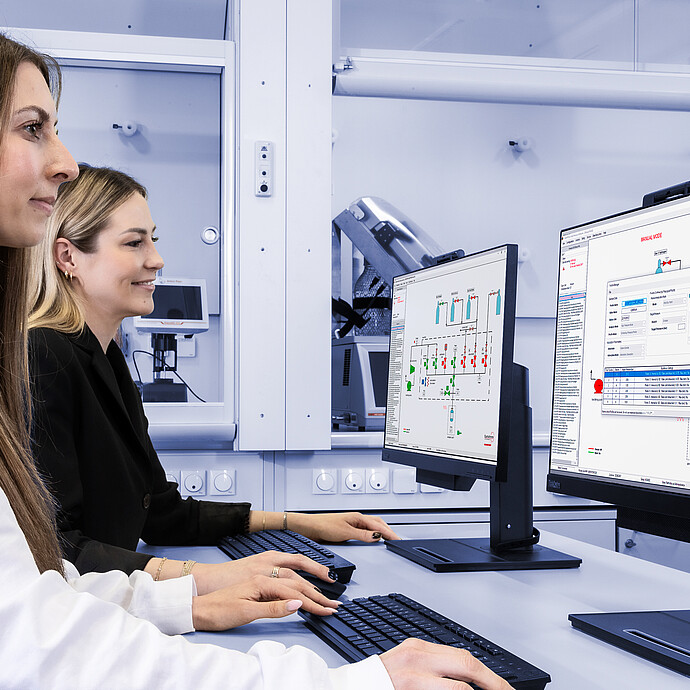 Two laboratory technicians operating computers displaying software interfaces for the Anton Paar iSorb HP high-pressure gas sorption analyzer. The screens show schematic diagrams of gas flow paths and system settings, highlighting precise control and monitoring capabilities for high-pressure gas sorption experiments. The lab environment includes advanced instrumentation in the background.