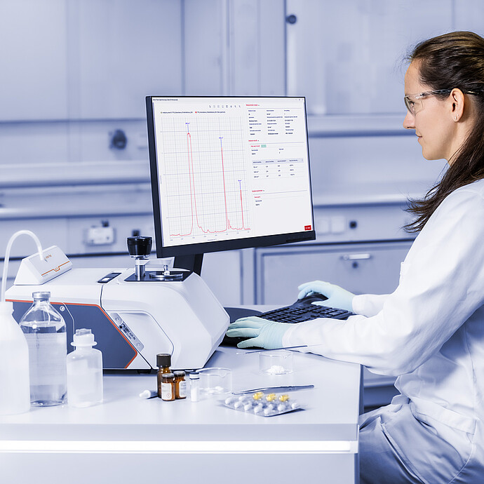 Laboratory technician operates the Anton Paar Lyza 3000 FTIR spectrometer while reviewing an infrared spectrum on a monitor.