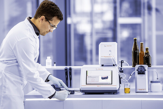 Lab technician using Anton Paar DMA 5002, Alcolyzer 3001, Xsample 3100, and Enzymatic Reader in a beer analysis laboratory.