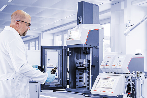 Technician places a bottle into the Anton Paar TPO 5000 system, connected with Carbo 520 Optical modules and Modulyzer setup in a lab environment.