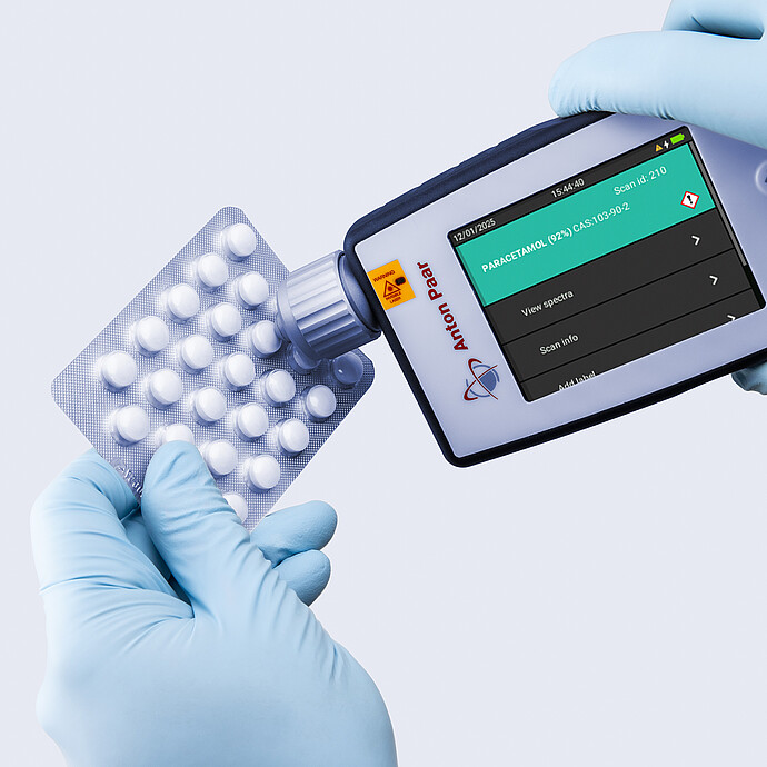 Two gloved hands using the Anton Paar Cora 100 handheld Raman spectrometer to identify tablets in a blister pack as paracetamol.
