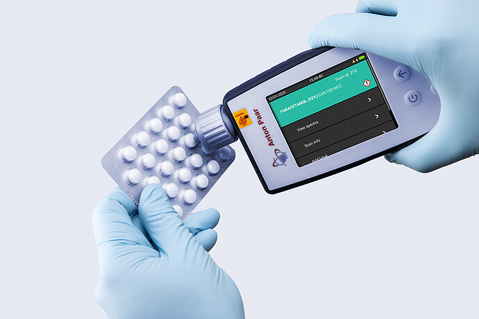 Two gloved hands using the Anton Paar Cora 100 handheld Raman spectrometer to identify tablets in a blister pack as paracetamol.