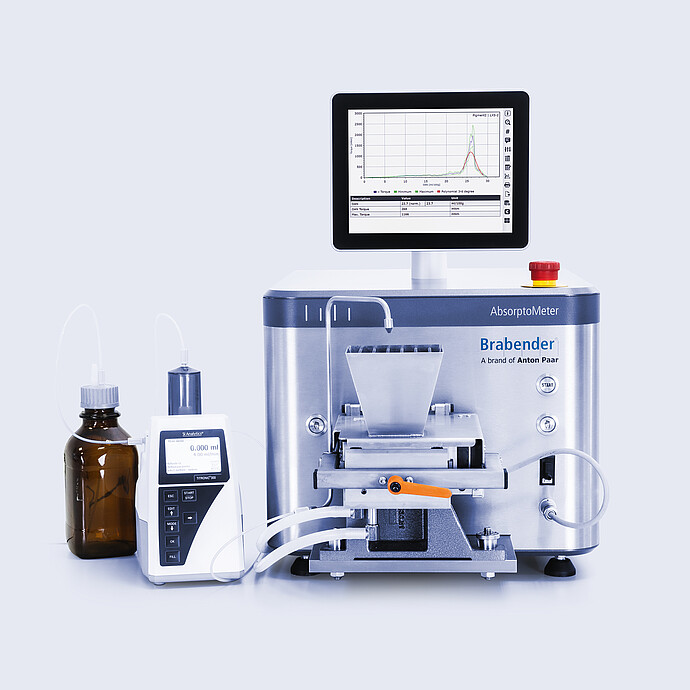 Brabender AbsorptoMeter with hopper and integrated display showing measurement curves, connected via tubing to a dosing unit and reagent bottle on a lab bench