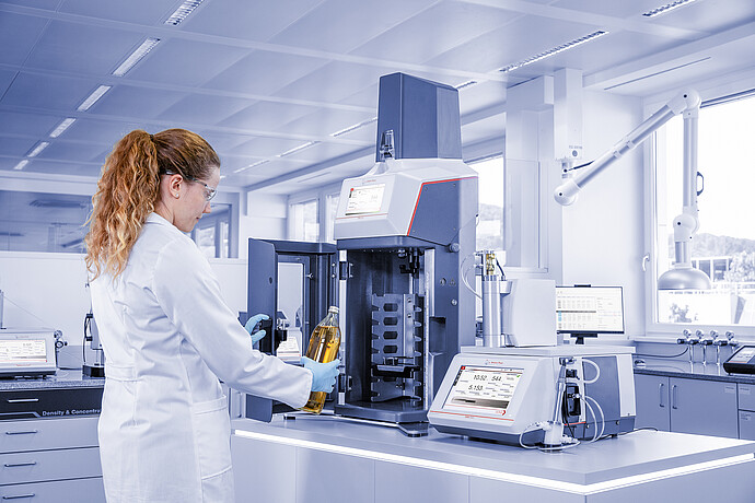 Laboratory technician loading soft drink bottle into Anton Paar TPO connected to DMA 5002 with Xsample in quality control lab