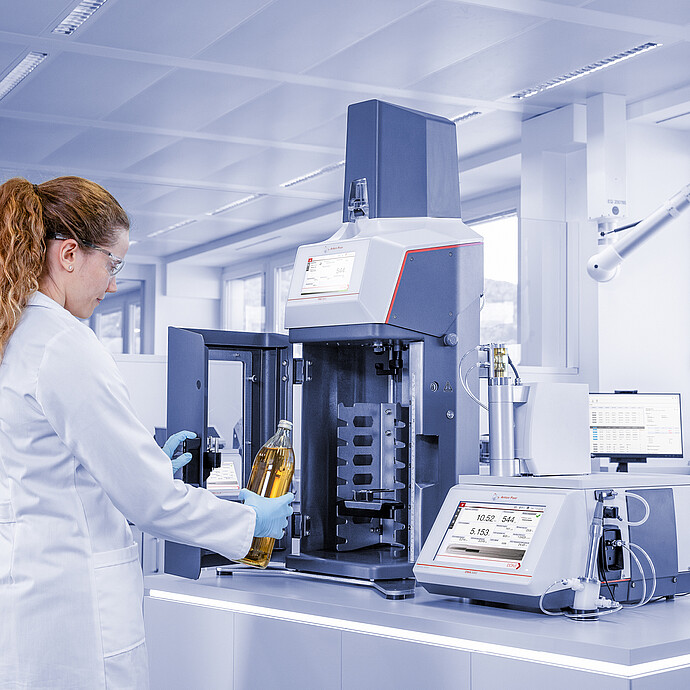 Laboratory technician loading soft drink bottle into Anton Paar TPO connected to DMA 5002 with Xsample in quality control lab