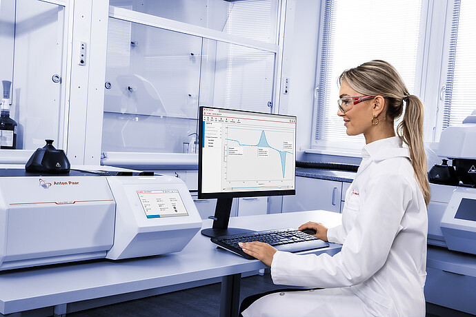 Technician operating Anton Paar Julia DSC 300 in laboratory, using Julia Suite on monitor displaying DSC measurement curve, with additional instrument in background