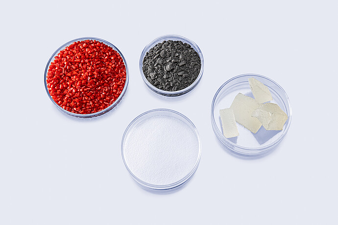 Four dishes containing red pellets, dark granules, white powder and pale solid samples for extensional rheology testing