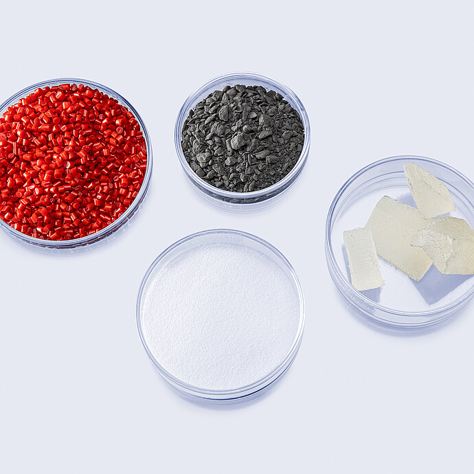Four dishes containing red pellets, dark granules, white powder and pale solid samples for extensional rheology testing