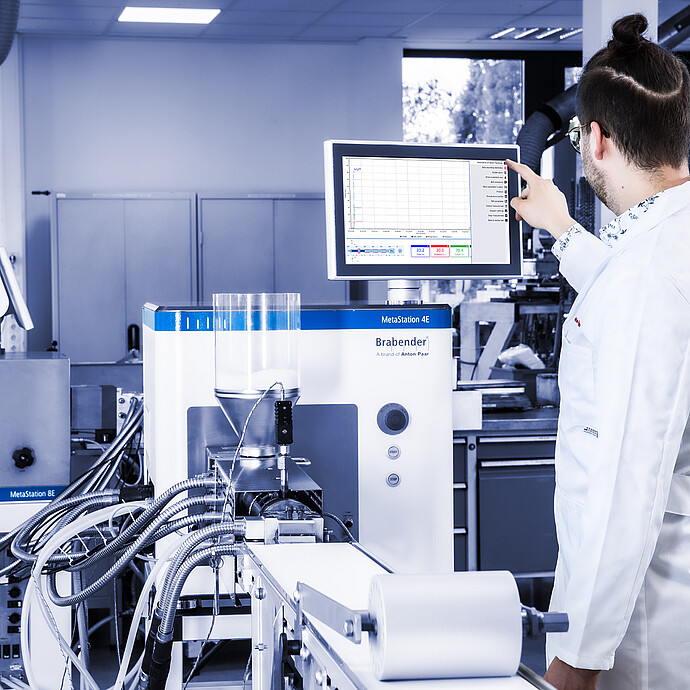 Laboratory technician operates a Brabender MetaStation 4E modular torque rheometer; a Brabender MetaStation 8E is visible beside it.