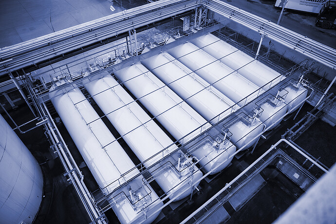 Aerial view of an industrial tank farm with multiple horizontal storage vessels arranged in parallel, connected by piping, valves, and elevated pipe racks