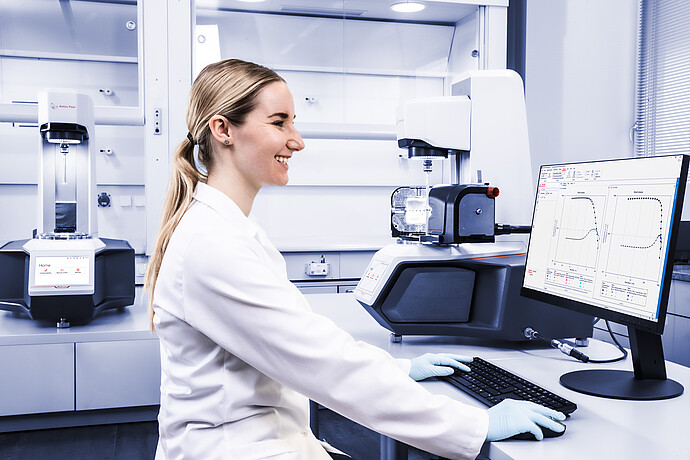 Technician using RheoCompass software beside two Anton Paar Modular Compact Rheometer MCR instruments in a lab