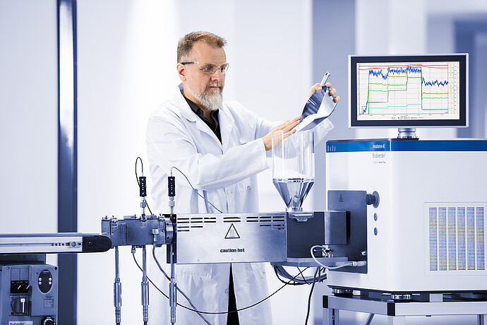 Technician pours pellets into the feed hopper of a Brabender MetaStation 8E modular torque rheometer with graph display.