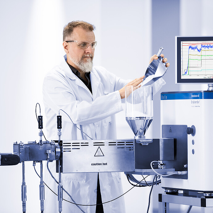 Technician pours pellets into the feed hopper of a Brabender MetaStation 8E modular torque rheometer with graph display.