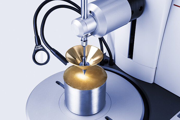 Close-up of Anton Paar Penetrometer PNR 500 with brass cone penetrating translucent amber sample in metal cup under focused lighting.