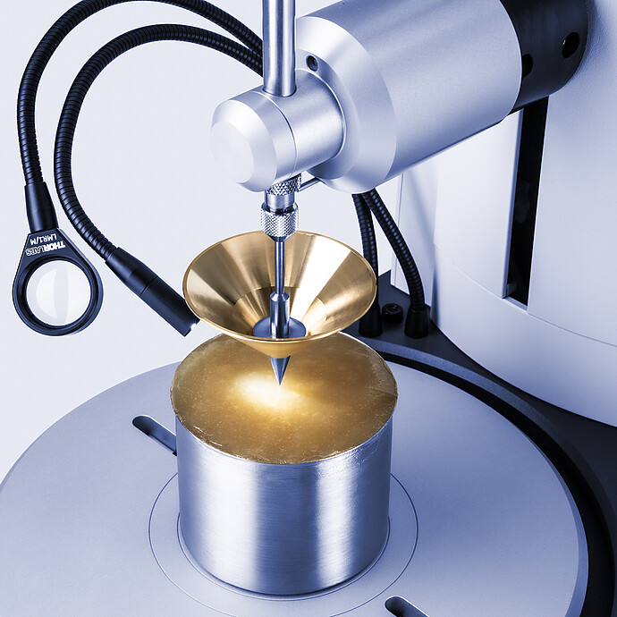 Close-up of Anton Paar Penetrometer PNR 500 with brass cone penetrating translucent amber sample in metal cup under focused lighting.