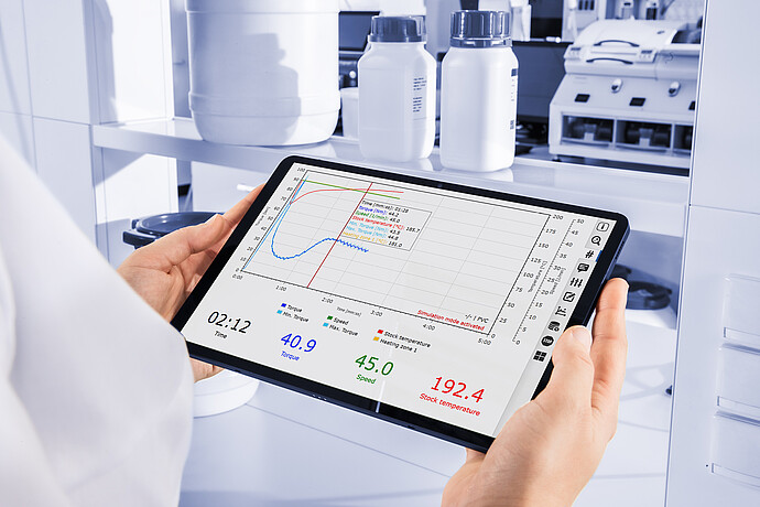Laboratory technician reviews Brabender MetaStation torque, speed, and stock-temperature curves on a tablet beside sample containers.