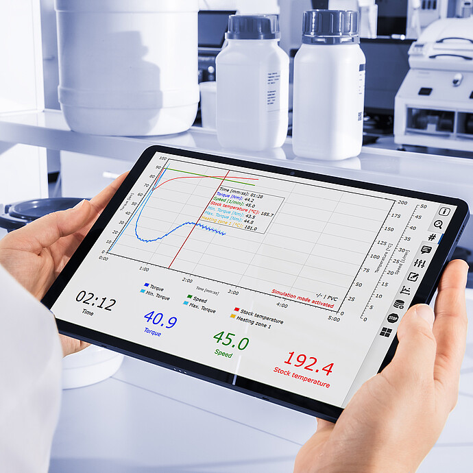 Laboratory technician reviews Brabender MetaStation torque, speed, and stock-temperature curves on a tablet beside sample containers.