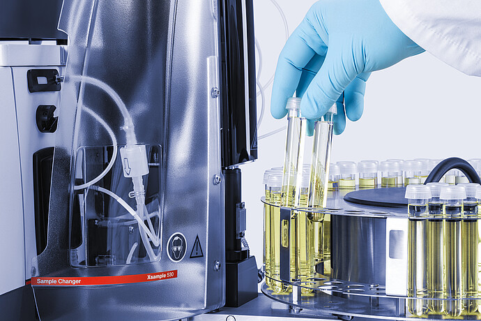 Gloved technician placing sample vials in the Anton Paar Xsample 530 sample changer carousel beside clear cover and tubing