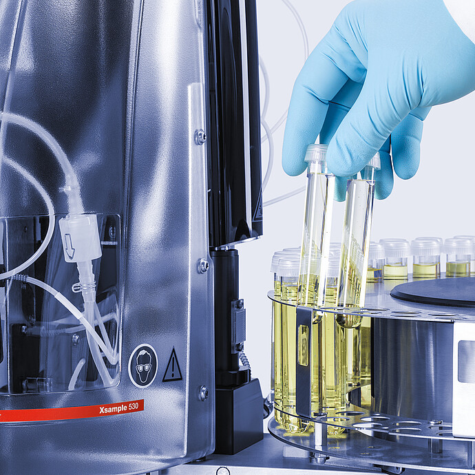 Gloved technician placing sample vials in the Anton Paar Xsample 530 sample changer carousel beside clear cover and tubing
