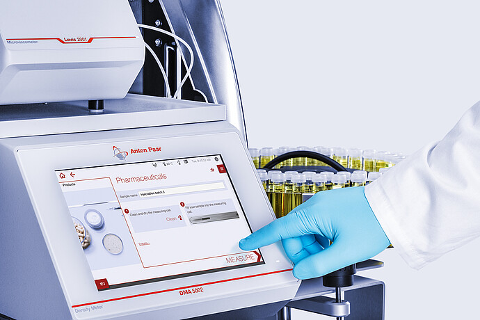 Gloved technician taps Measure on Anton Paar DMA 5002 screen with Lovis 2001 and Xsample 530 vial carousel