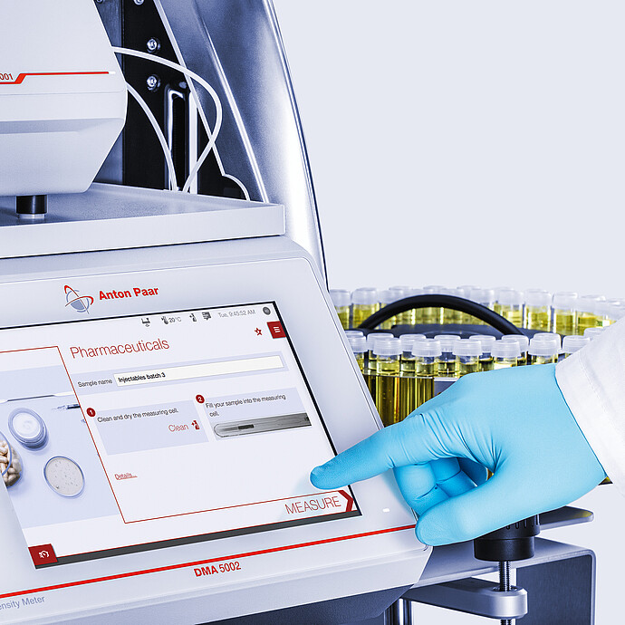 Gloved technician taps Measure on Anton Paar DMA 5002 screen with Lovis 2001 and Xsample 530 vial carousel