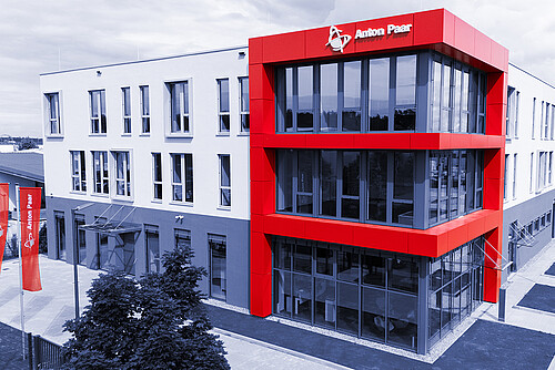 Modern exterior view of the Anton Paar ProveTec building in Blankenfelde-Mahlow, Germany, with red facade elements and large glass windows.