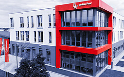Modern exterior view of the Anton Paar ProveTec building in Blankenfelde-Mahlow, Germany, with red facade elements and large glass windows.
