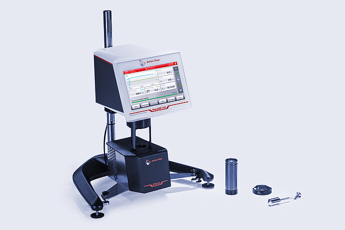 Three-quarter front view of the ViscoQC 300 rotational viscometer with the PTD 80 Peltier temperature device, with accessories laid out beside the base on a light blue background