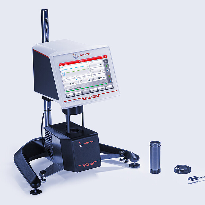 Three-quarter front view of the ViscoQC 300 rotational viscometer with the PTD 80 Peltier temperature device, with accessories laid out beside the base on a light blue background