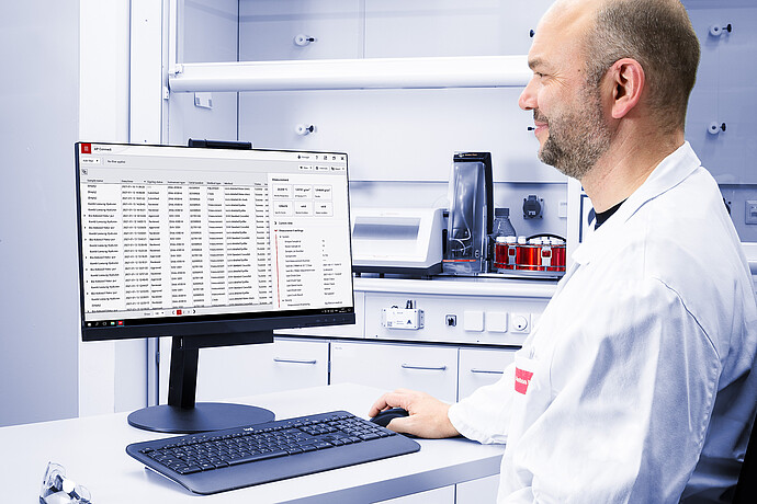 Technician using AP Connect on a monitor, with Anton Paar RTD Measurement System and red sample vials in the lab background.