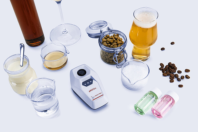 Anton Paar pH2Go digital pH meter placed among beverages, food ingredients, and buffer solutions, illustrating pH measurement across different liquid samples.