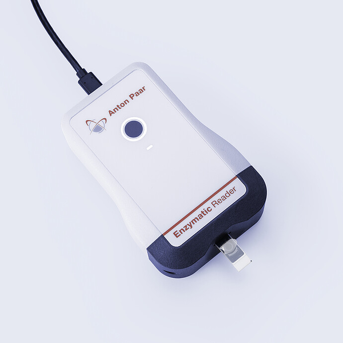 Anton Paar Enzymatic Reader digital ethanol meter with inserted test strip, illuminated button, and USB cable on gray background.