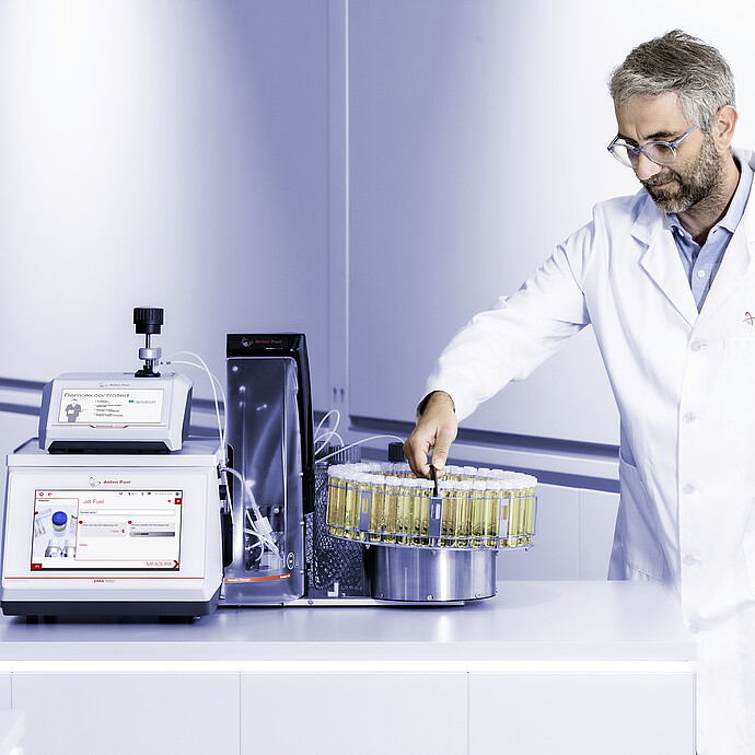Lab technician handling vial carousel beside Anton Paar DMA 5002 with Lovis 2000 M/ME and Xsample 530 sample changer