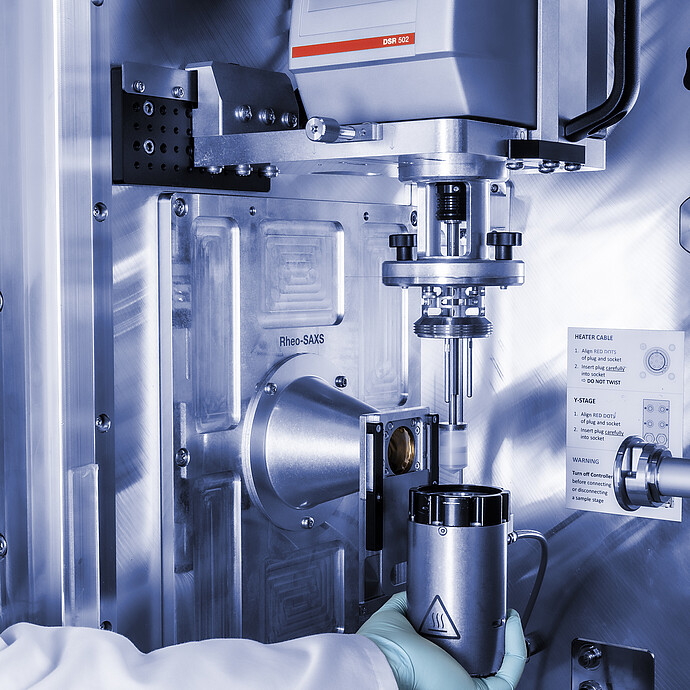 Anton Paar DSR 502 measuring head in a Rheo-SAXS setup, with a gloved technician positioning a cylindrical component