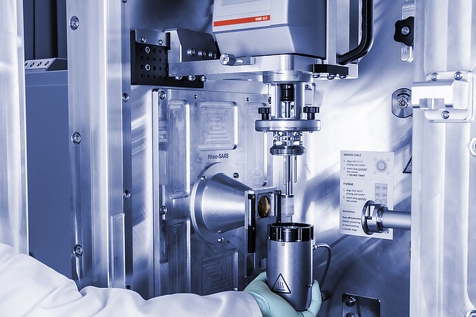 Anton Paar DSR 502 measuring head in a Rheo-SAXS setup, with a gloved technician positioning a cylindrical component