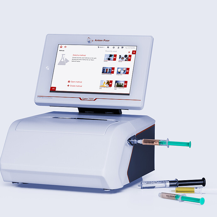 Anton Paar Lyza 7000 FTIR spectrometer with touchscreen, connected flow cell, and several syringes on a light gray background.
