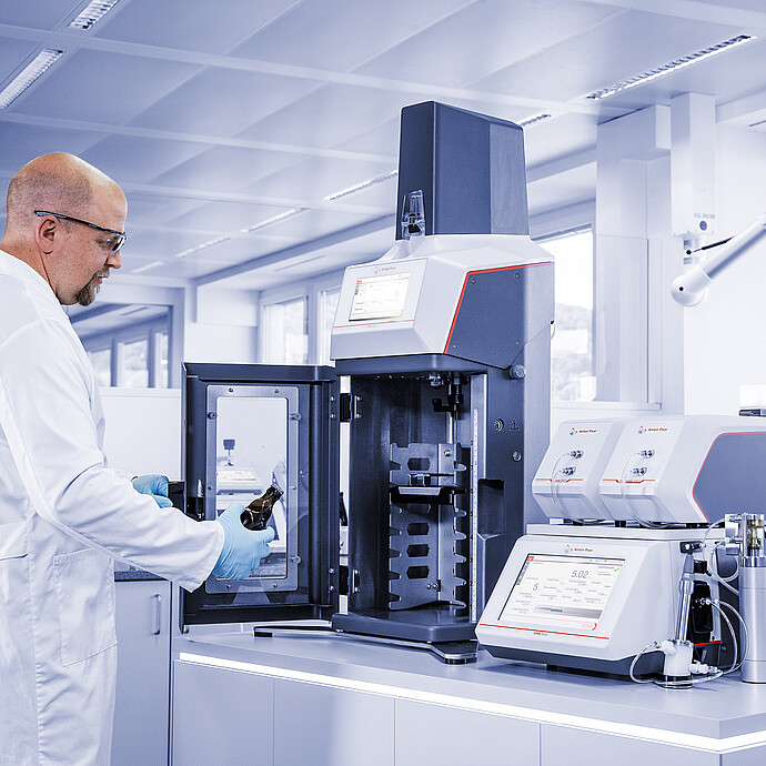 Technician loading beer bottle into Anton Paar TPO connected to DMA 5002 with Alcolyzer and Haze modules in laboratory