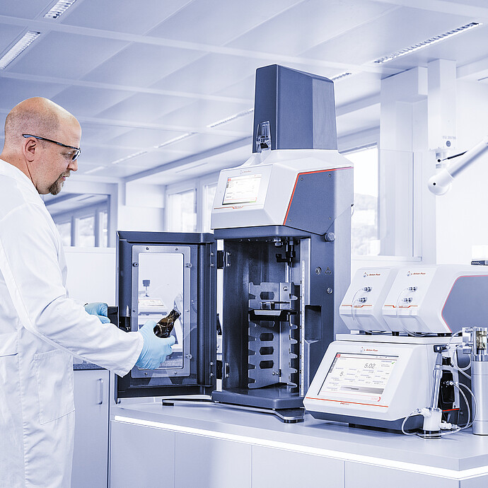 Technician loading beer bottle into Anton Paar TPO connected to DMA 5002 with Alcolyzer and Haze modules in laboratory
