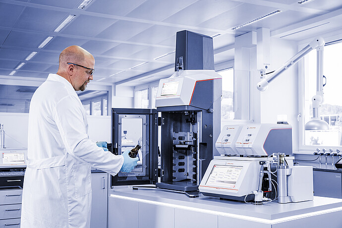 Technician loading beer bottle into Anton Paar TPO connected to DMA 5002 with Alcolyzer and Haze modules in laboratory