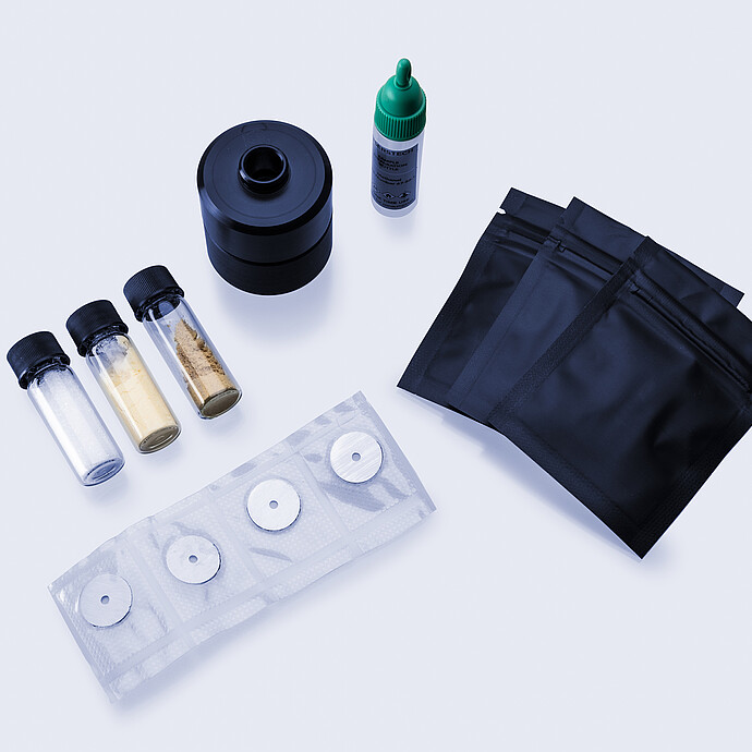 Assorted reference materials including vials with powders, sealed black pouches, a dropper bottle, a sampling accessory, and circular calibration targets.