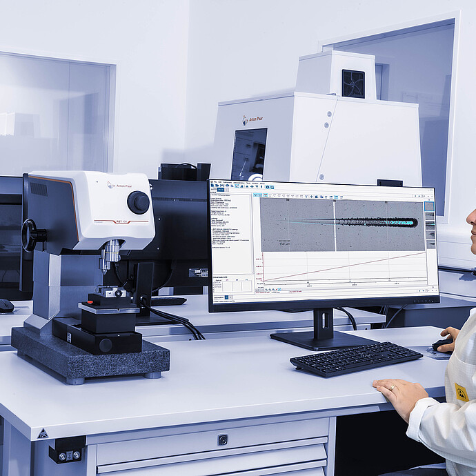 A technician operating the Anton Paar Revetest® Scratch Tester RST 100 in a laboratory, reviewing scratch test data displayed on a computer monitor.